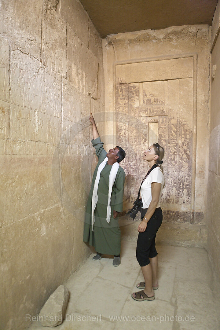 Waerter zeigt Touristin Inschrift an einer Mastaba bei Stufenpyramide Sakkara des Pharao Djoser