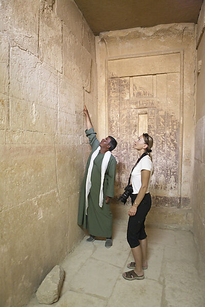 Waerter zeigt Touristin Inschrift an einer Mastaba bei Stufenpyramide Sakkara des Pharao Djoser